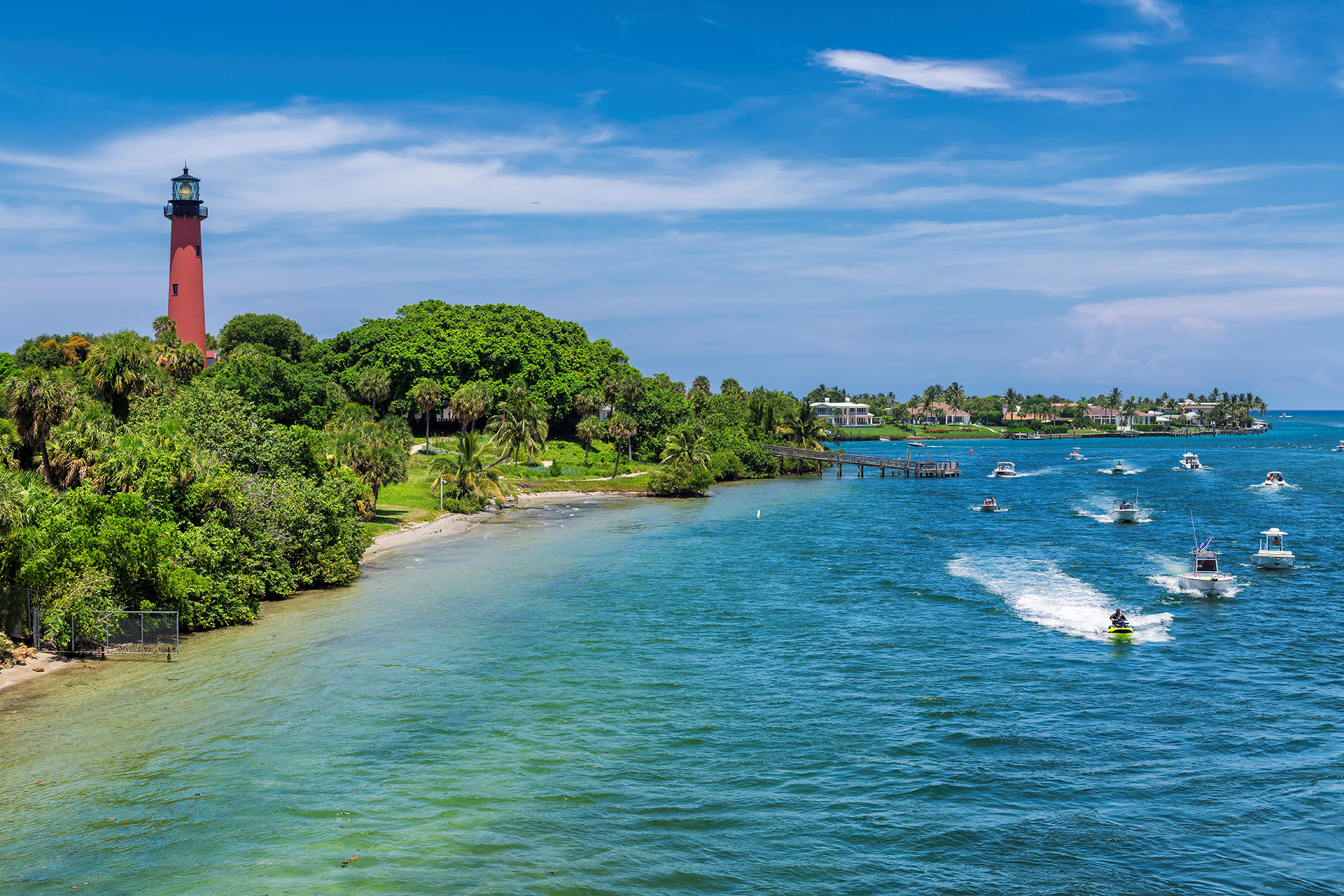 The image depicts a scenic view of a river with boats and a lighthouse in the background, surrounded by palm trees and a blue sky.