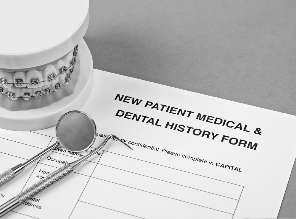 Alt text   A photograph of a document with the title  NEW PATIENT MEDICAL HISTORY   DENTAL HISTORY  prominently displayed, accompanied by a pair of scissors and a small dental model.