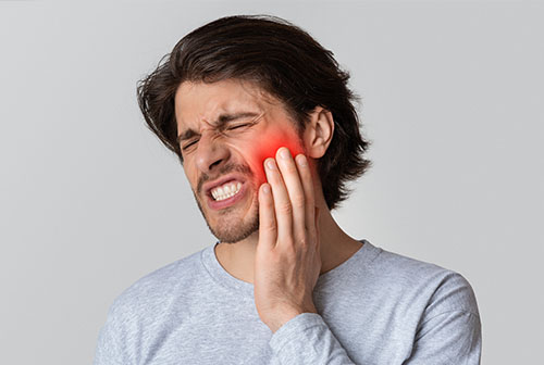 A man with a toothache grimaces while holding his face with his hand.