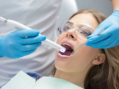 The image shows a dental professional using a device to clean a patient s teeth during a dental appointment.